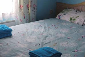 Una cama con ropa de cama floral, una colcha azul y un almohadón con diseño de pájaro.