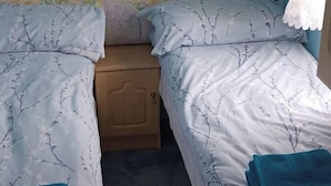 A twin bed with a floral pattern, a wooden nightstand, and a blue towel. - Donegal Coastal Mobile Homes with Private Garden (Letterkenny)