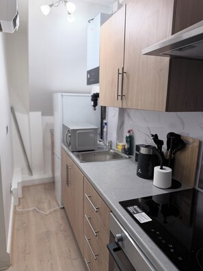 A compact kitchen with wooden cabinets, a built-in microwave, a sink, and a black induction cooktop. - Flat in Central London 10 mins London Bridge (London)