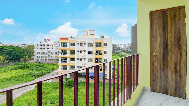 A balcony with a view of a multi-story residential building, a green landscape, and a clear sky. - Collection O Eco Park Kolkata (Barasat)