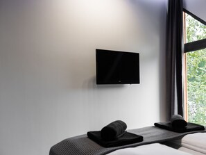 A modern hotel room with a flat-screen TV mounted on the wall, a bed with a dark headboard, and a window with a view of greenery. - in Niechorze mit Großem Grill by Interhome (Niechorze)