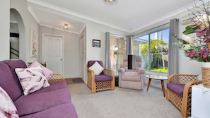 A living room with a purple sofa, wicker chairs, a small table, and a view of the outdoors through large windows. - Morpeth Cottage | In the hear of Morpeth (Morpeth)