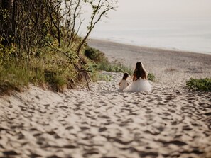 En sandstrand med vegetation på vänster sida och en fri utsikt över havet i bakgrunden.