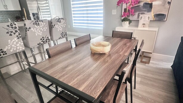 Un comedor con una mesa y sillas de madera, una cocina al fondo y un cuadro abstracto grande en la pared.