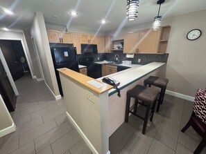 Une cuisine moderne avec un îlot central, des meubles en bois, un réfrigérateur noir et une horloge au mur.