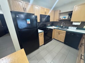 A kitchen with wooden cabinets, a black refrigerator, a stove, a sink, and a dishwasher. - Wake up to the sunrise from your balcony - Oceanfront 1 BR condo Pono Kai Kapa'a (Kapaʻa)