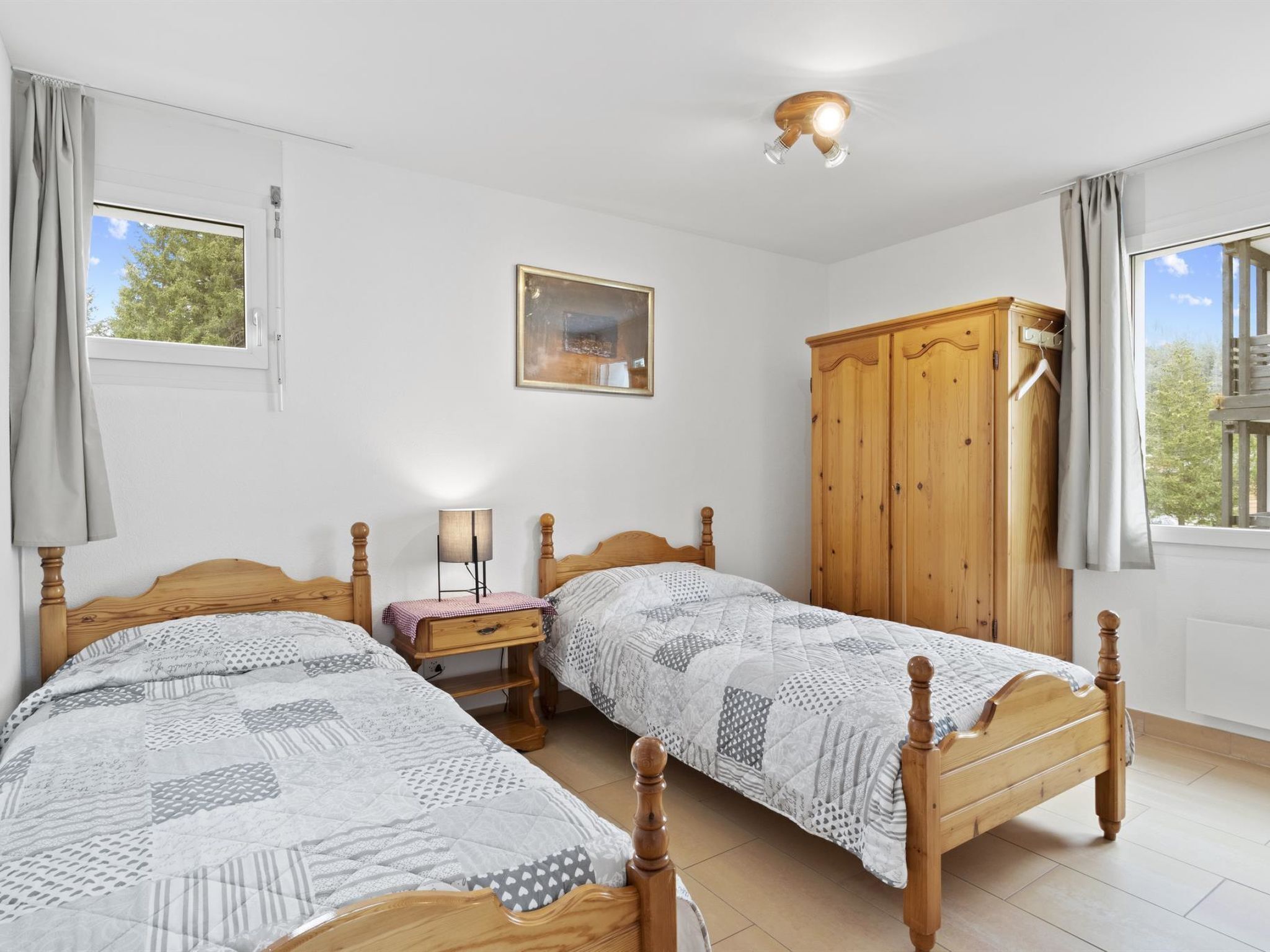 Un dormitorio con dos camas de madera, una mesita de noche con lámpara, un armario y un cuadro en la pared.
