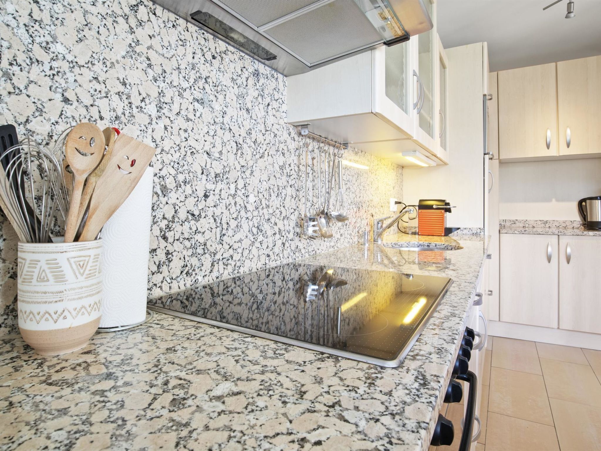 Eine Küche mit einer Granit-Arbeitsplatte, einem Edelstahl-Spülbecken und Holzkochlöffeln in einem dekorativen Behälter.