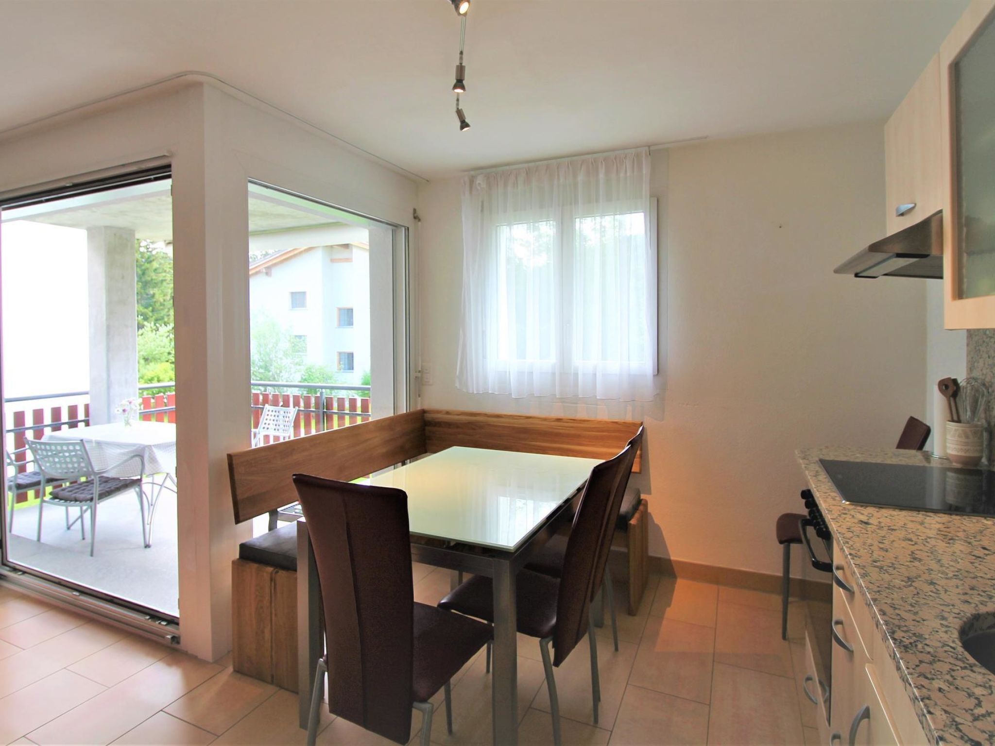 Une cuisine moderne avec un coin repas, de grandes fenêtres et une vue sur un bâtiment à l’extérieur.