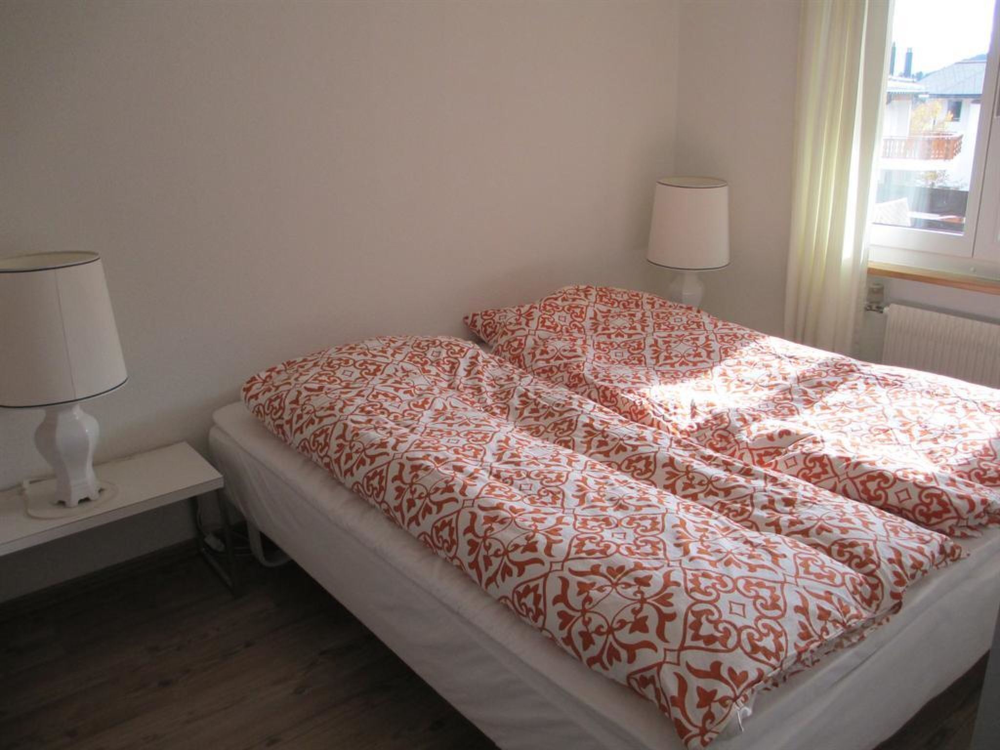 Un dormitorio con cama, dos lámparas de noche, una ventana con cortinas y un radiador.