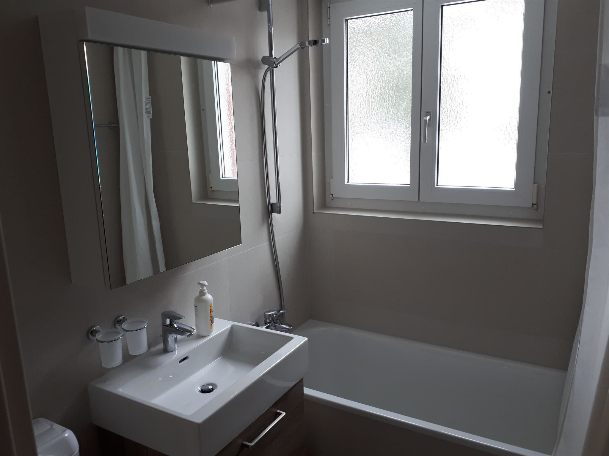 Une salle de bain avec un lavabo blanc, un miroir et une fenêtre.