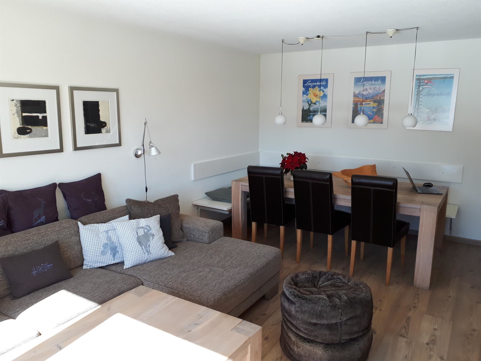 Una sala de estar moderna con un sofá, una mesa de comedor con sillas y una computadora portátil sobre la mesa.