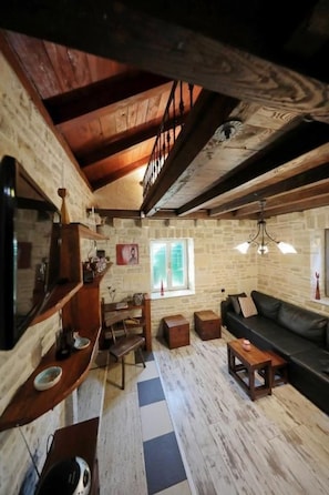 A rustic interior with exposed wooden beams, a black leather sofa, and a stone wall. - Olive Garden Paljka by Interhome (Donje Rastane)