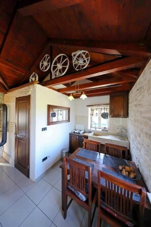 A rustic kitchen with wooden beams, a dining table with chairs, and a stone wall. - Olive Garden Paljka by Interhome (Donje Rastane)