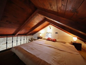 A bedroom with a sloped ceiling, a bed, two bedside tables with lamps, and a window with curtains. - Olive Garden Paljka by Interhome (Donje Rastane)