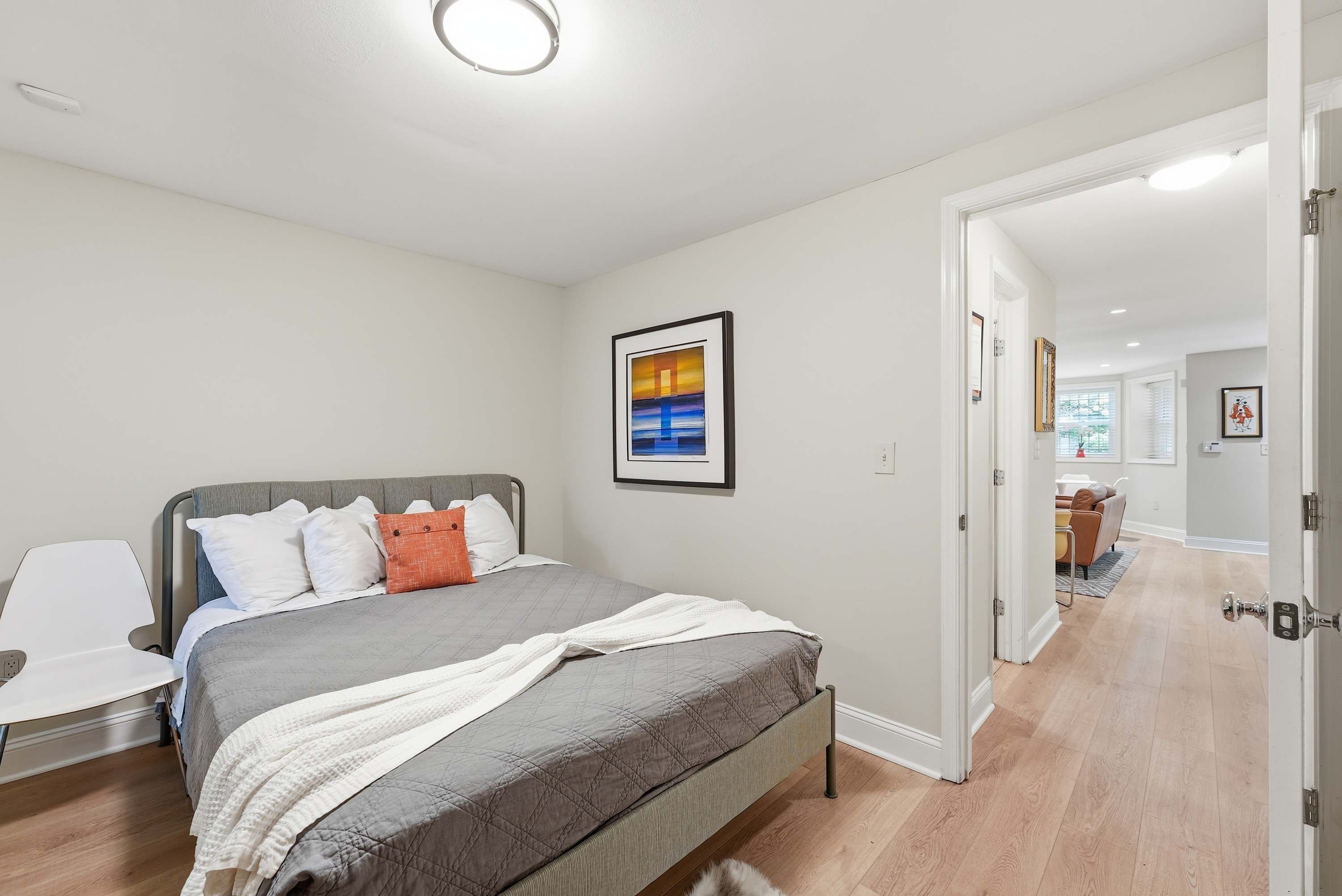 A bedroom with a bed, a bedside table, a chair, and a door leading to another room.
