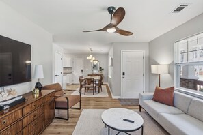 A modern living room with a flat-screen TV, a sofa, a coffee table, and a dining area with a chandelier. - Bright & Stylish Bungalow near Uptown - 4BR 2B& Fenced in Backyard! (Charlotte)