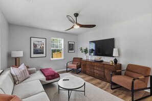 Een moderne woonkamer met een bank, fauteuils, een salontafel, een televisie en kunstwerken aan de wanden.