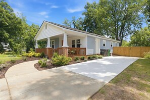A single-story house with a front porch, a driveway, and a fenced yard. - Bright & Stylish Bungalow near Uptown - 4BR 2B& Fenced in Backyard! (Charlotte)
