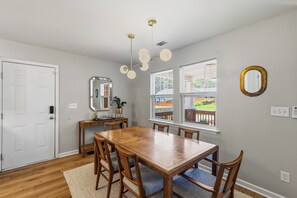 A dining room with a wooden table and chairs, a mirror, and a ceiling light fixture. - Bright & Stylish Bungalow near Uptown - 4BR 2B& Fenced in Backyard! (Charlotte)