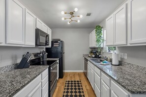 A kitchen with white cabinets, a black refrigerator, a microwave, and a granite countertop. - Bright & Stylish Bungalow near Uptown - 4BR 2B& Fenced in Backyard! (Charlotte)