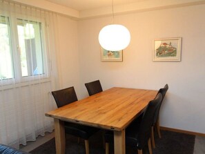 Ein Essbereich mit Holztisch, vier Stühlen, einer Hängelampe und zwei gerahmten Bildern an der Wand.