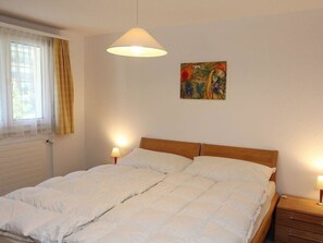 Ein Schlafzimmer mit einem Doppelbett, zwei Nachttischen, einem fensterbelaubten Fenster und einem Bild an der Wand.