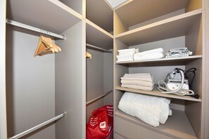 Ein Hotelkleiderschrank mit Regalen, auf denen gefaltete Handtücher, eine rote Einkaufstasche und ein weißer Transportheizkörper liegen.