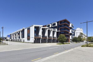 Een modern meerlaags gebouw met een combinatie van balkons en ramen, een heldere lucht en een verharde weg met een fietspad.