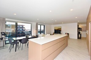 A modern apartment with a large kitchen island, dining area, and a view of the cityscape through large windows. - Luxury Central City Sub Penthouse (Christchurch)