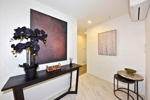 A modern interior with a large abstract painting, a console table with decorative items, and a small round table with a marble top. - Luxury Central City Sub Penthouse (Christchurch)