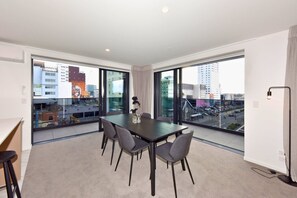 Ein modernes Hotelzimmer mit großem Balkon, einem Esstisch mit Stühlen und Blick auf die Stadt.