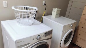 A laundry area with a front-loading washer and dryer, a white laundry basket, and a trash can. - Casa Bearclaw Family Getaway Disney4 Miles 2 bedroom/2bathroom Pet Friendly (Kissimmee)