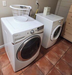 A laundry area with a front-loading washer and dryer, a white laundry basket, and a trash can. - Casa Bearclaw Family Getaway Disney4 Miles 2 bedroom/2bathroom Pet Friendly (Kissimmee)