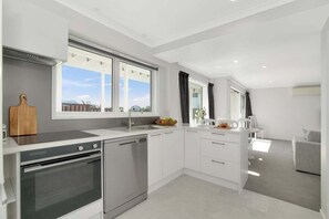 A modern kitchen with a built-in oven, a dishwasher, and a large window providing a view of the outdoors. - The Seaway Vista (Tauranga)