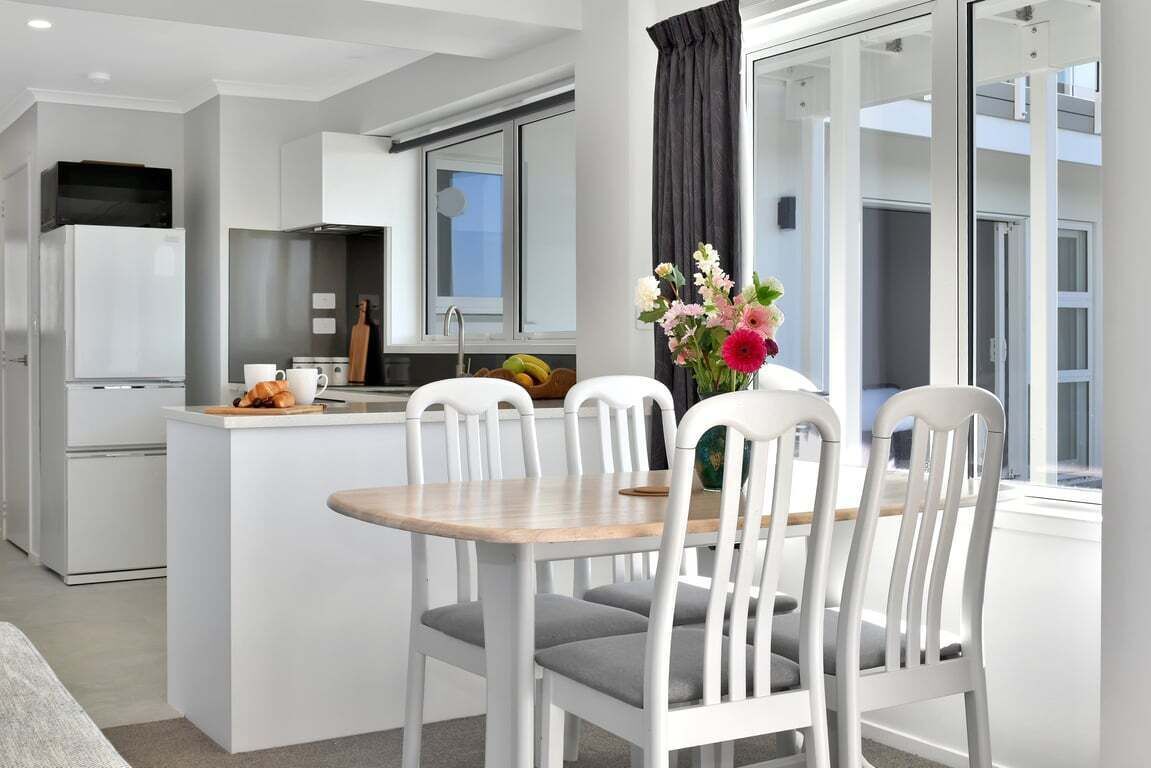A modern kitchen with white cabinetry, a central island with seating, and a view of the outside through large windows.