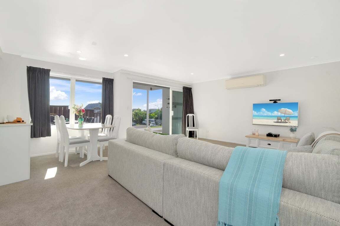 Un salon moderne avec un canapé, une table à manger et des chaises, et un téléviseur fixé au mur.