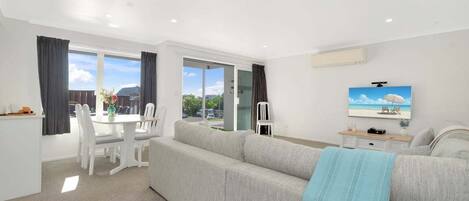 Una sala moderna con un sofá, una mesa de comedor con sillas y un televisor en la pared.
