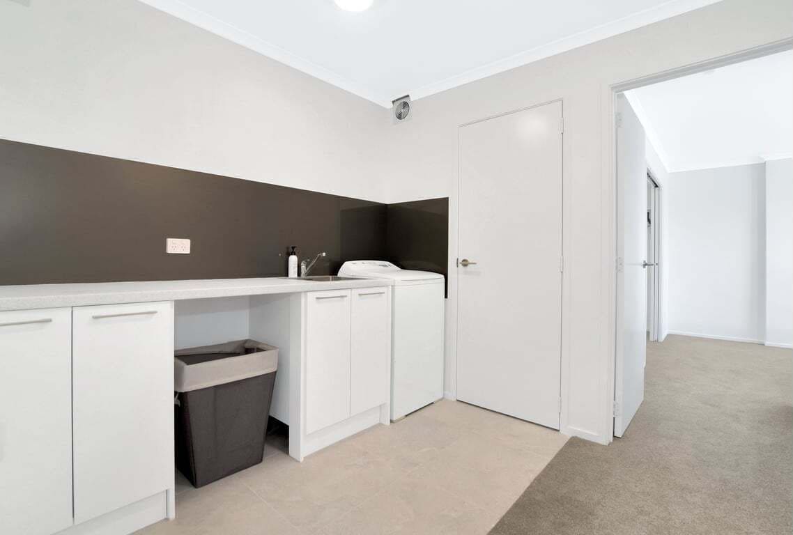 Una habitación moderna y bien iluminada con una kitchenette blanca, un bote de basura y una puerta que da a otra área.