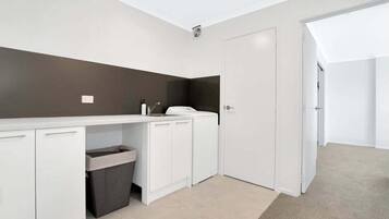 A modern, well-lit room with a white kitchenette, a trash bin, and a door leading to another area.