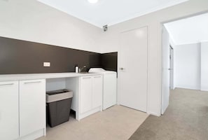 A modern, well-lit room with a white kitchenette, a trash bin, and a door leading to another area. - The Seaway Vista (Tauranga)