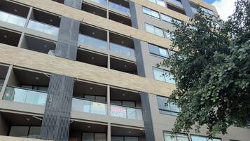 A multi-story building with a modern design, featuring balconies, large windows, and a gated entrance.