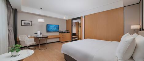 A hotel room with a large bed, a desk with a chair, a television, and a small table with a plant.