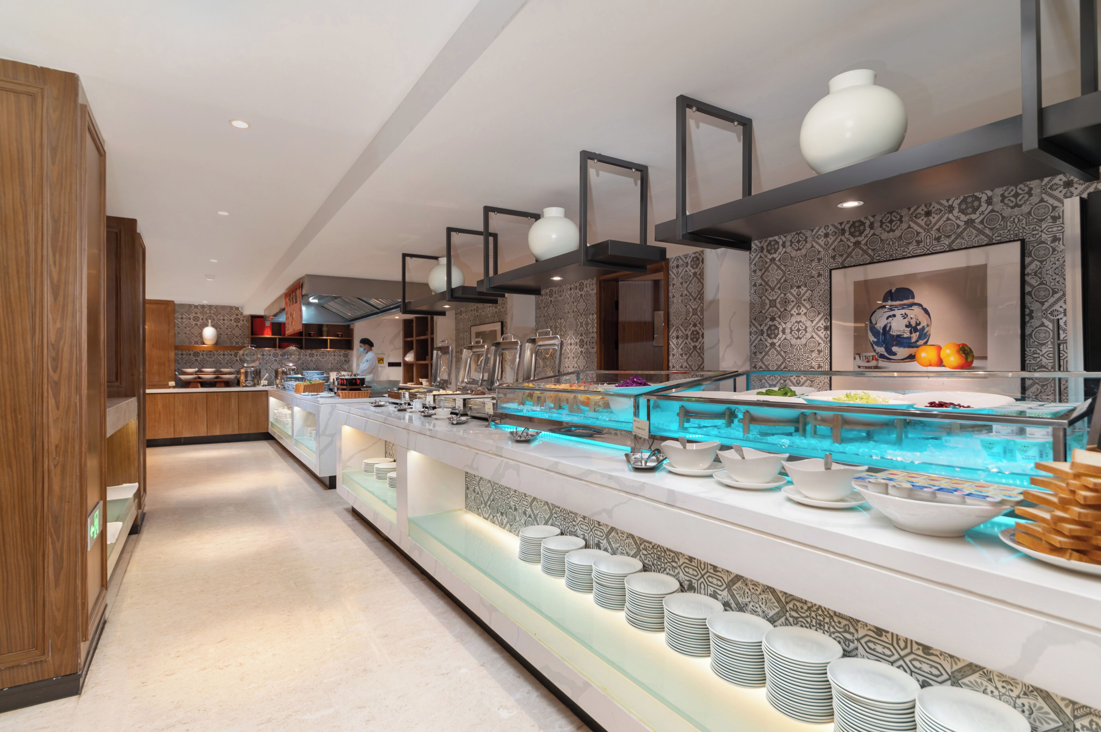 Uma área de buffet com diversas opções de comida, incluindo uma vitrine de vidro para sobremesas e uma seção com tigelas e pratos para servir.
