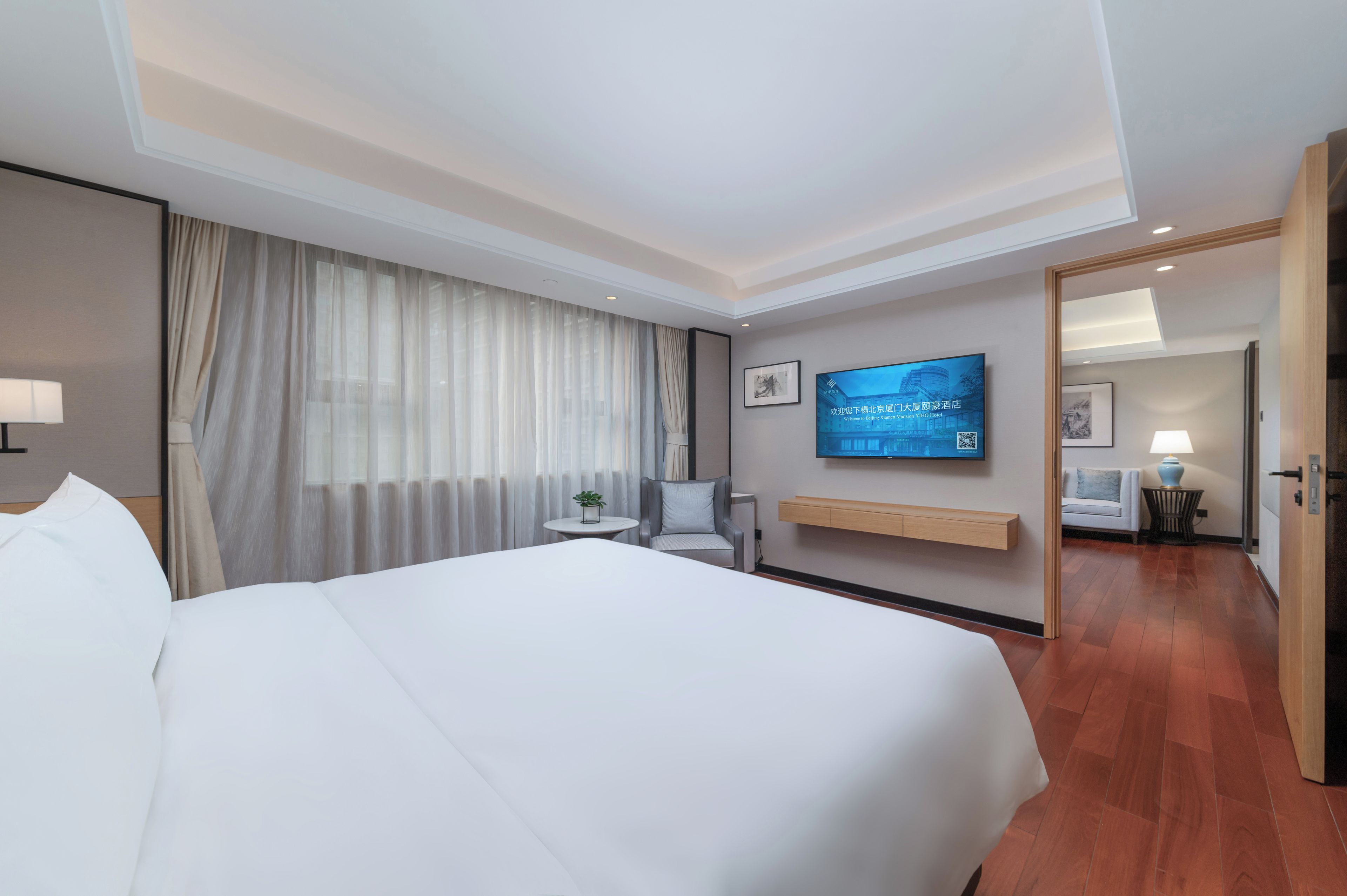 Habitación de hotel con una cama grande, un televisor montado en la pared, una mesita de noche con una lámpara y vistas al pasillo.