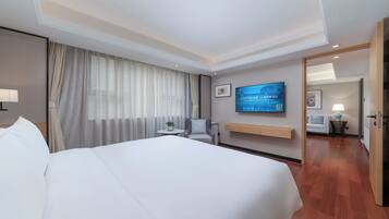 Habitación de hotel con una cama grande, un televisor montado en la pared, una mesita de noche con una lámpara y vistas al pasillo.