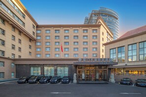 Un hôtel doté d’une façade moderne, d’une grande entrée et d’un parking où sont stationnées plusieurs voitures.