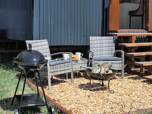 An outdoor seating area with wicker chairs, a grill, and a fire pit.