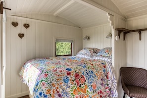 A bedroom with a floral bedspread, a window with a view of greenery, and a wooden chair.