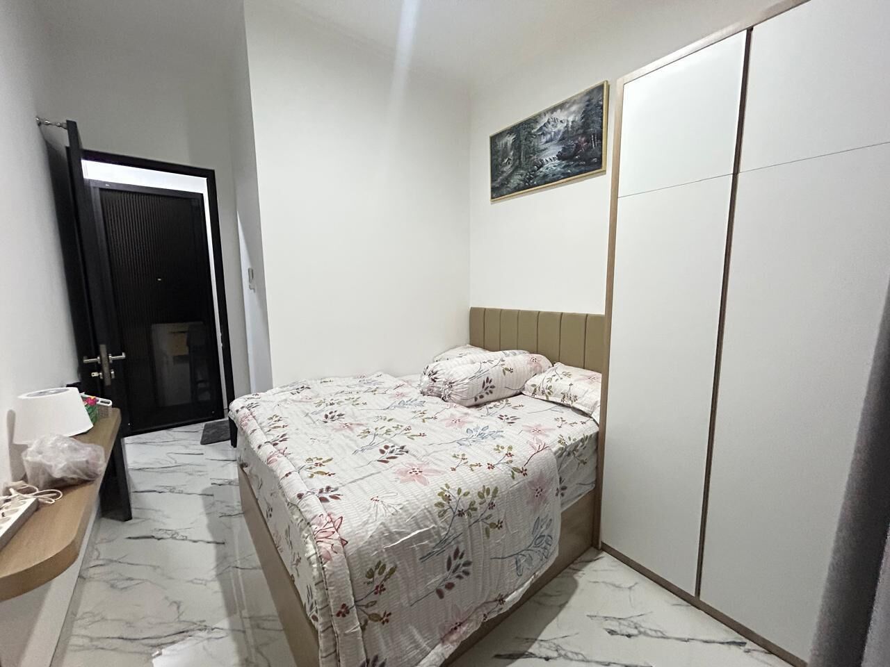 Een slaapkamer met een bed, een kledingkast, een schilderij aan de muur en een deur naar een andere kamer.